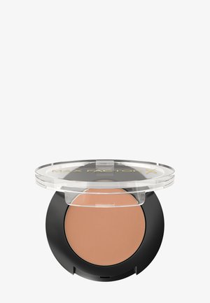 Poudre compacte avec un couvercle transparent et une base noire, présentant une surface lisse et marron clair. L'étiquette indique "MAX FACTOR X" en doré.