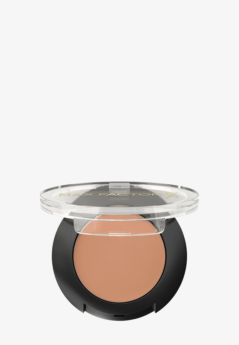 Poudre compacte avec un couvercle transparent et une base noire, présentant une surface lisse et marron clair. L'étiquette indique "MAX FACTOR X" en doré.
