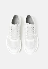 Bílé sportovní boty s prodyšným síťovým svrškem, strukturovanými detaily a polstrovanou podrážkou. Mají tkaničky a zesílenou oblast špičky.