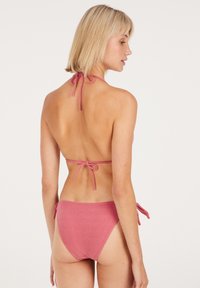 Różowy, materiałowy bikini z wiązaniami na szyi i bokach, o prostym designie i gładkiej fakturze. Widok z tyłu ukazuje minimalne zakrycie.