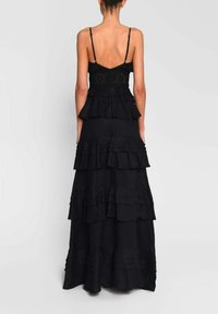 Sort kjole med lagdelte flæser, spaghetti stropper og en tætsiddende bodice med intrikate broderier. Glat tekstur og fuldlængde.