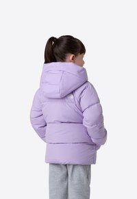 Vaaleanlaventelin värinen toppatakki hupulla, jossa on tikattu kuviointi ja harmaa logodetaili takana, yhdistetty harmaisiin collegehousuihin.