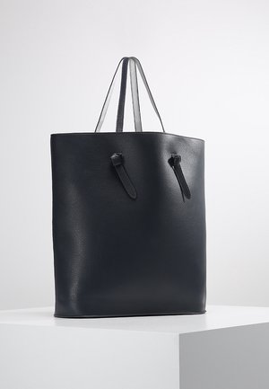 Sac cabas en cuir noir avec deux poignées supérieures, présentant une texture lisse et un design minimaliste. Comprend des sangles réglables pour un look polyvalent.