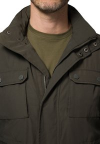 Kurtka w oliwkowym kolorze z zapięciem na zamek i zatrzaskami, z składanym kołnierzem oraz dwiema kieszeniami na piersi. Gładka, trwała faktura materiału.