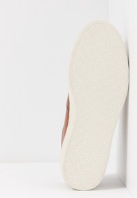 Braune Ledersneaker mit einer strukturierten weißen Gummisohle, die ein Diamantmuster aufweist. Die Seitenansicht zeigt klare Linien und detaillierte Nähte.