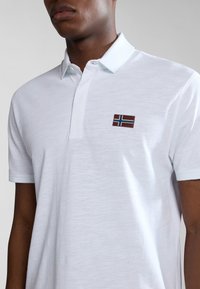 Polo bianco realizzato in tessuto strutturato con colletto a bottoni, dotato di una piccola bandiera norvegese ricamata sul petto.