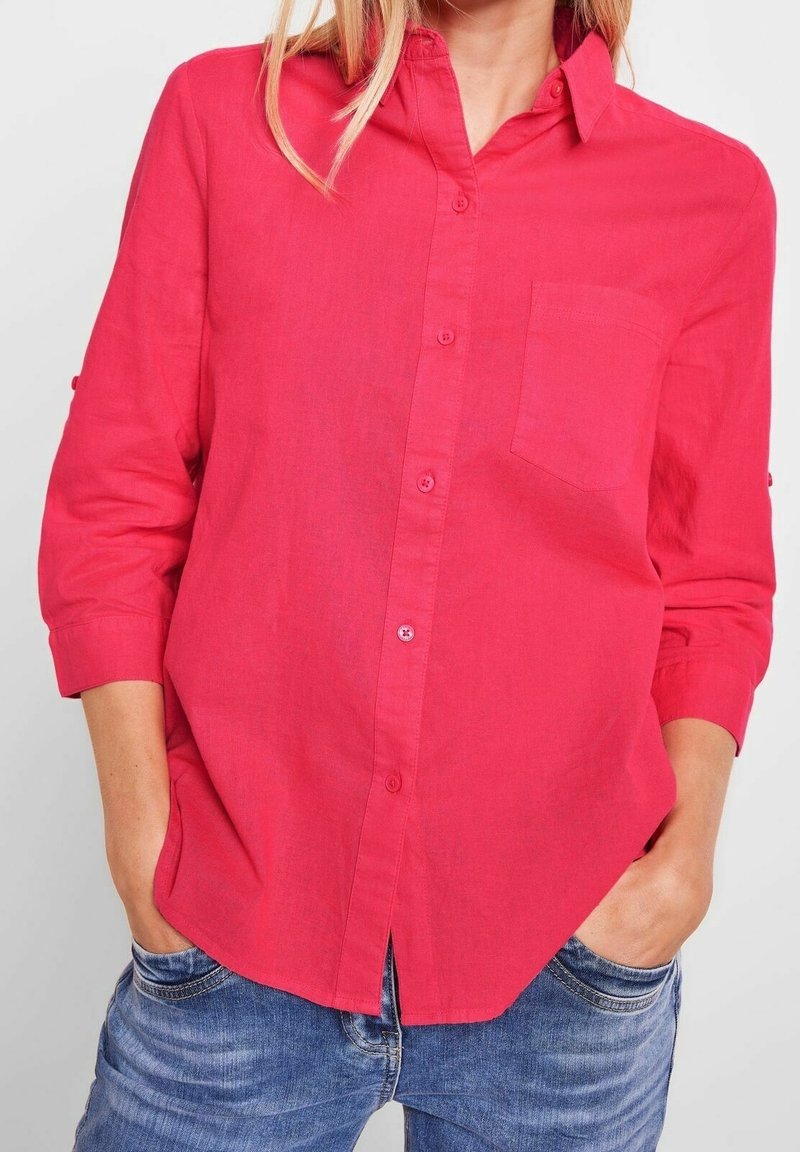 Chemise rose à manches longues et avec poche sur la poitrine, fabriquée dans un tissu léger. La chemise a une coupe décontractée et un design simple.
