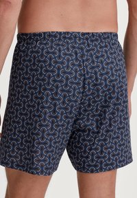 Shorts da nuoto blu navy con un motivo a spirale ripetuto in bianco, arancione e azzurro chiaro. Vita elastica, tessuto leggero, lunghezza a metà coscia.