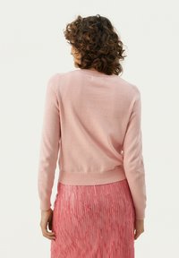 Light pink sweater made of soft knit fabric with a round neck and ribbed hem, paired with a textured pink skirt featuring horizontal patterns.