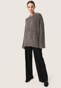 Grå fuzzy sweater med bred udskæring, lange ærmer og ribbet kant, parret med sorte vide bukser og mørke sko.