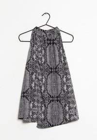 Haut dos nu noir et blanc avec un motif imprimé serpent, présentant un aspect texturé et un design fluide, suspendu à un cintre en métal noir.