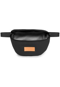 Sac à taille en tissu noir avec fermeture éclair ouverte, sangle ajustable et écusson rectangulaire marron à l'avant.