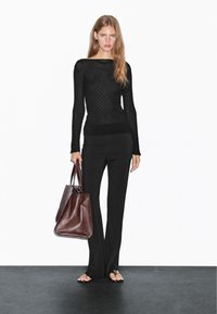 Black knitted long-sleeve top with a textured pattern, paired with black fitted pants and a brown leather tote bag.