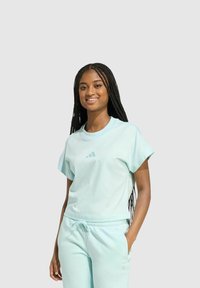 Conjunto de top corto de color verde azulado y pantalones deportivos, con mangas cortas, cuello de barco y un sutil logo de tres rayas en el pecho.