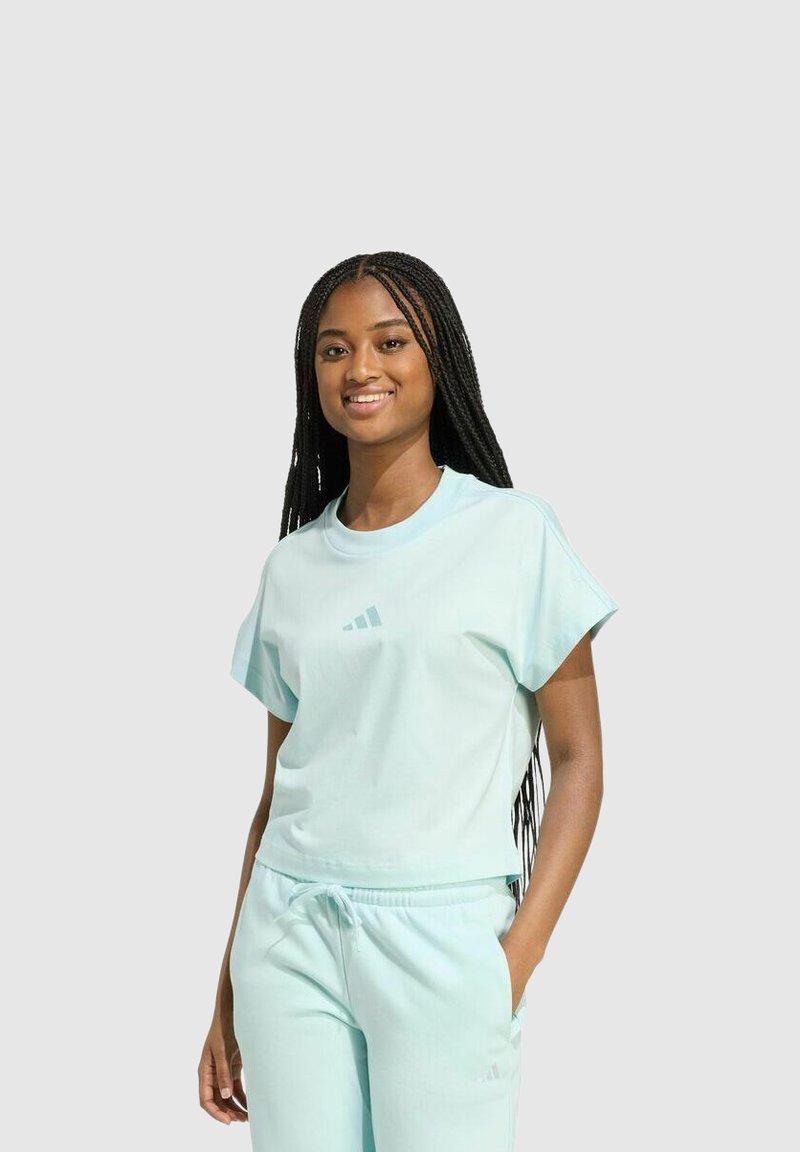 Conjunto de top corto de color verde azulado y pantalones deportivos, con mangas cortas, cuello de barco y un sutil logo de tres rayas en el pecho.