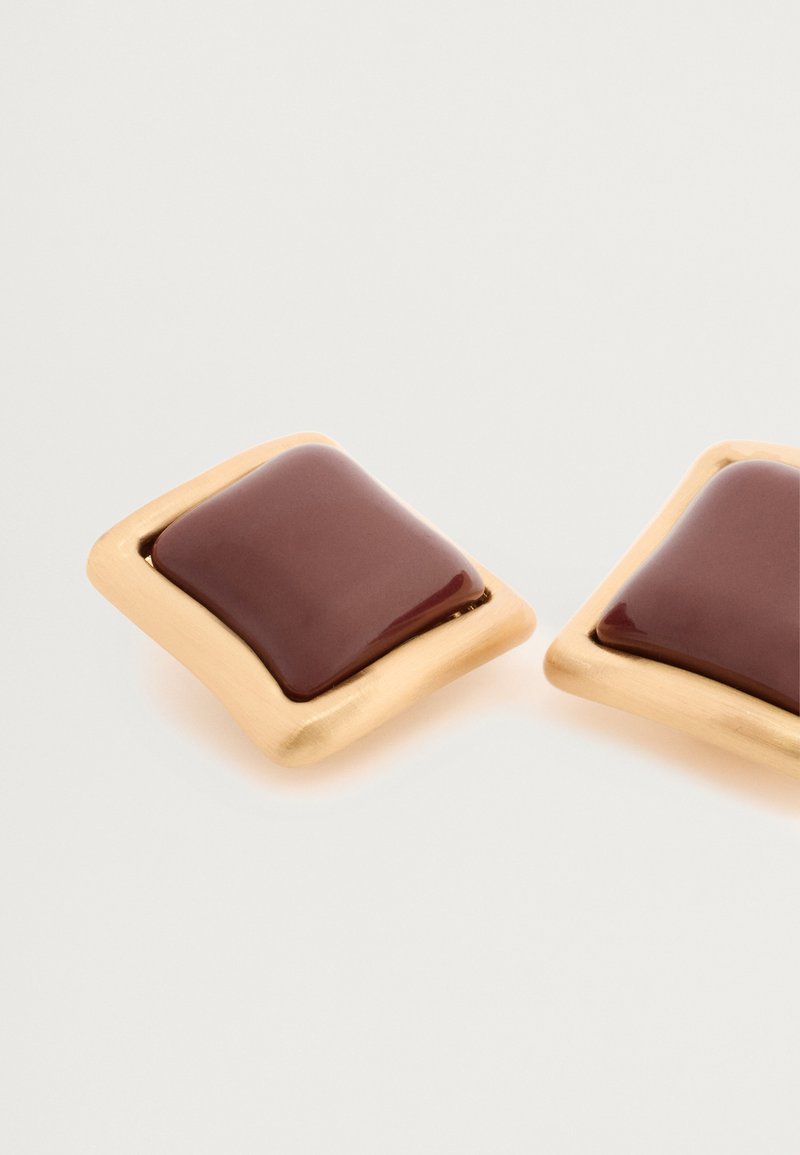 Vierkante oorbellen met een glanzend bruine center, omringd door een gestructureerde goudkleurige metalen rand, voorzien van gladde lijnen en gepolijste oppervlakken.