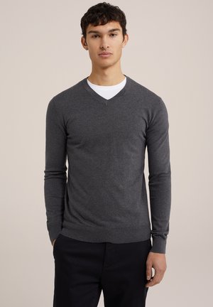 Grauer Wollpullover mit V-Ausschnitt, langen Ärmeln und geripptem Saum. Getragen über einem weißen T-Shirt mit Rundhalsausschnitt. Einfaches Design, glatte Textur.