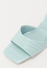 Un sandalo in finta pelle di coccodrillo blu chiaro con punta quadrata e ampia cinghia, con una soletta in tessuto liscio e un design a tacco basso.
