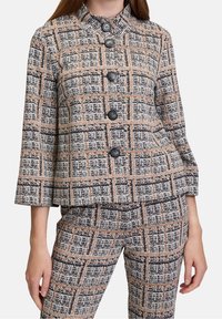 Vävd kavaj i ett strukturerat tyg med ett rutmönster i beige, svart och rostfärger, med sex svarta knappar och kinesisk krage.