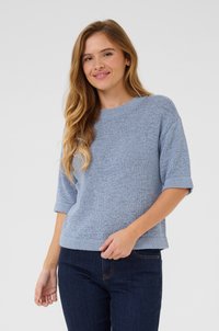 Pull en tricot bleu clair avec un col rond et des manches courtes retroussées. Tissu texturé, coupe décontractée, associé à un jean en denim foncé.
