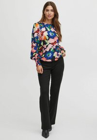 Floral long-sleeve blouse in blue, pink, and green on a dark background. Features gathered cuffs and a relaxed fit. Paired with black trousers.