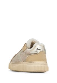Tan en beige sneaker met een textiel bovenwerk, gouden metallic accenten, een zachte binnenvoering en een gegroefde rubberen zool. Klittenbandsluiting.