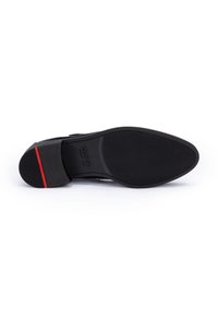 Schwarze Schuhsohle mit einer strukturierten Oberfläche, die einen glatten schwarzen Absatz und einen roten Akzentstreifen aufweist. Die Formen sind schlank und zeitgemäß.