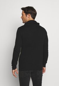 Suéter negro de punto con cuello alto y mangas largas; tejido texturizado, diseño ajustado y puños y bajo acanalados.