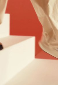 Footwear on steps, featuring a cream shoe with textured material, paired with beige pants. The background is a bright red.