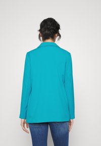 Tyrkysový blazer s klopovým límečkem a dlouhými rukávy, s rovný střih, který se na pase zužuje, hladká textura, minimální detaily.