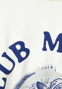 Bílý bavlněný tričko s výrazným modrým textem, který říká "CLUB" a "M", s grafickým designem ryby pod ním. Textura je hladká.