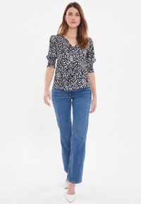 Sort bluse med hvide polkaprikker, V-hals design, puffede ærmer, parret med lyseblå lige ben jeans og hvide spidse hæle.