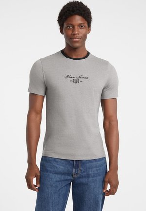 Tricou gri cu mânecă scurtă și guler negru, având logo-ul "Guess Jeans" în negru pe piept. Material din bumbac neted, design ajustat.