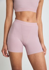 Pantaloni corti elasticizzati di un delicato rosa chiaro con cintura alta, caratterizzati da una costruzione senza cuciture e dettagli di cucitura sottili per un comfort e una flessibilità ottimali.