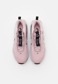 Zapatillas deportivas de color rosa claro con un upper texturizado, que presentan cordones negros y etiquetas de marca. Punta redondeada y acentos de suela negra.