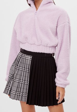Lichtpaarse fleece trui met hoge kraag, cropped lengte, gecombineerd met een zwarte geplooide rok met een geruit patroon aan één kant.