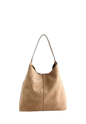 Frau mit langen dunklen Haaren, die ein schwarzes schulterfreies Oberteil und einen braunen Rock trägt und eine große hellbraune Wildleder-Schultertasche trägt.