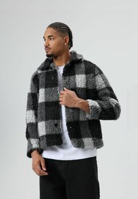 Geruite fleecejas in zwart, grijs en wit, met een gestructureerd oppervlak, grote knopen en een kraag.