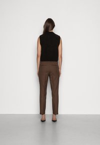 Svart ärmlös stickad topp som kombineras med bruna skräddarsydda byxor. Byxorna har en dragsko i midjan och två bakfickor. Släta texturer.