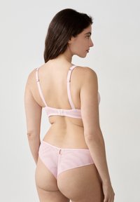 Lichtroze beha en bijpassende slipset. Zachte stof met verstelbare bandjes en een haaksluiting. De slip heeft een sleufdetail aan de achterkant.
