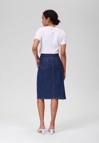 Jeans blyantskjørt i mørkeblå, mellomlangt med kontraststing, sidelommer og en tettsittende midje. Kombinert med en enkel hvit t-skjorte.
