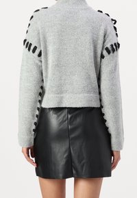 Pull gris court avec des accents de ruban noir le long des manches, présentant une finition texturée. Associé à une mini-jupe en cuir noir.