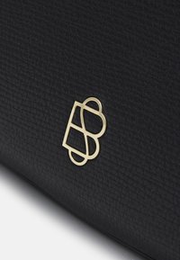 Sort struktureret lædertaske med et abstract logo i guldtoner. Logoet har afrundede kanter og indeholder elementer, der ligner bogstaverne B og D.