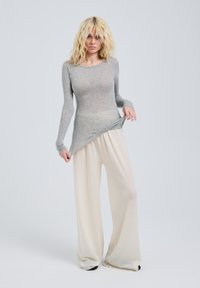 Top grigio a maniche lunghe realizzato in materiale trasparente abbinato a pantaloni crema a gamba larga, morbidi e sientiti; cuciture piatte e silhouette rilassata.