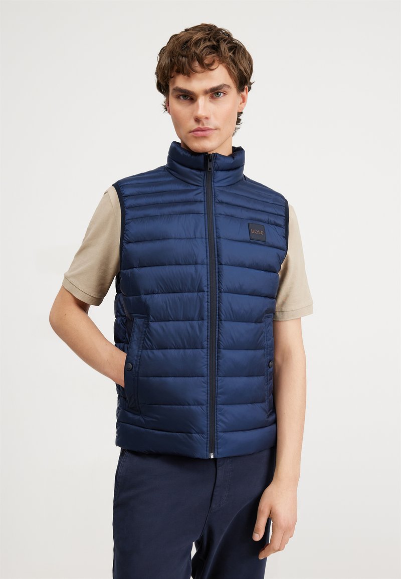 Gilet imbottito blu navy con colletto alto, caratterizzato da un motivo a righe orizzontali, tasche laterali e un piccolo patch con logo sul petto.