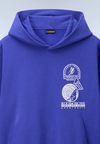 Felpa viola in morbido tessuto con ampio tascone frontale. Presenta loghi stampati bianchi: "Research Program" e "Napapijri". Vestibilità standard con cappuccio regolabile.