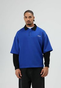 Blauw poloshirt met een zwarte kraag en grote mouwen, voorzien van een knoopsluiting met drie knopen en een klein logodetail op de borst.