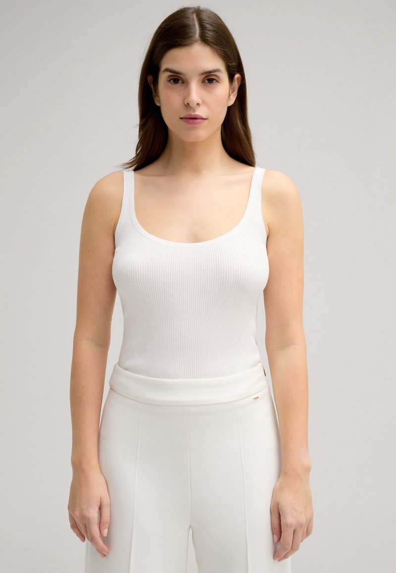 Canotta bianca a costine con spalline larghe, caratterizzata da un collo a giro. Abbinata a pantaloni bianchi su misura, con una texture liscia e design minimalista.