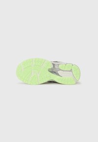 Semelle d'une basket grise et métallique avec une semelle à motif vert vif, montrée à l'envers sur un fond gris clair uni.