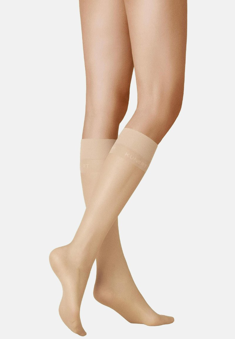 Beige kniehohe Kompressionsstrümpfe aus transparenter Material, mit glatter Textur und elastischen Bändern, auf denen "KUNERT" in Weiß gedruckt ist.